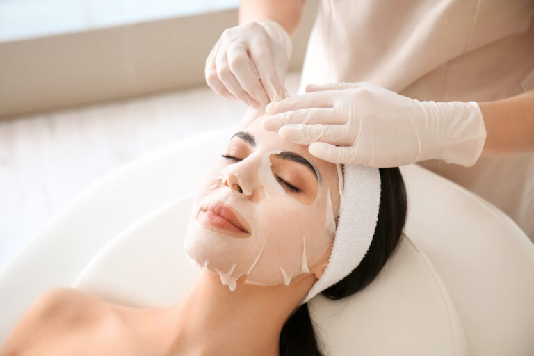 Cosmetologist,Applying,Sheet,Mask,On,Woman's,Face,In,Beauty,Salon
