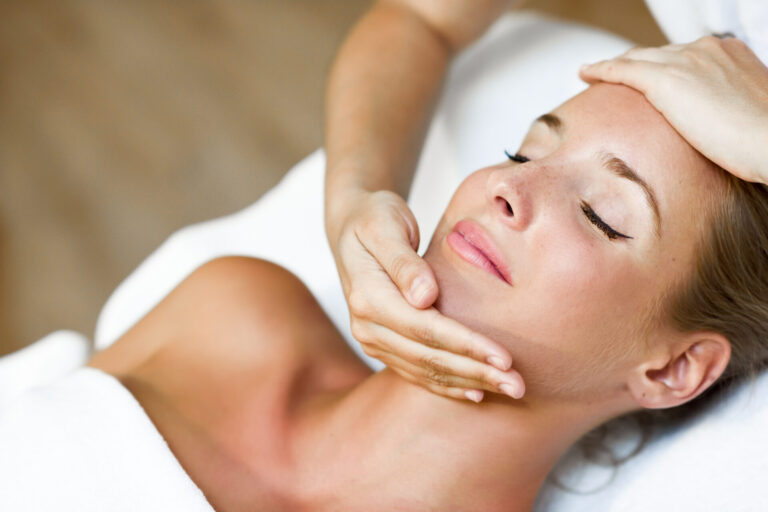 Young blond woman receiving a head massage in a spa center with eyes closed. Female patient is receiving treatment by professional therapist.
